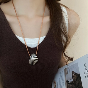 Close-up of a silver shell pendant necklace on a braided cord worn by a model