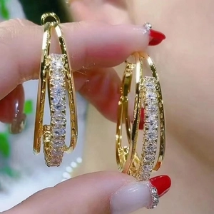 Detail of gold layered hoop earrings with zircon inlay held by a model for scale