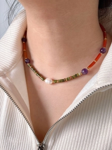 Detail of colorful bohemian stone beaded necklace with a central white pearl on a model