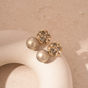 Detailed close-up of champagne gold earrings with rhinestones and faux pearls on a stone