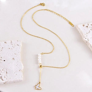 Gold necklace with white butterfly pendant and four pearls on a stone background