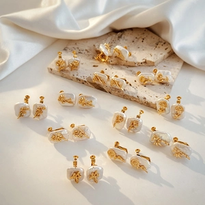 Macro detail of Chinese style gold floral earrings with baroque pearls on white silk