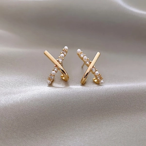 Detail of gold X-shaped earrings with pearls and crystals on champagne silk background