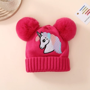 Detail of knit child's hat with unicorn embroidery and pink faux fur double pom-poms