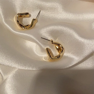 Detailed view of irregular gold circular earrings on white silk fabric background