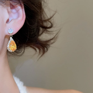 Close-up of sparkling gold drop earring with yellow gemstone on model's ear