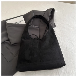 Flat lay of a black faux suede tote bag styled on a grey blazer for office aesthetic