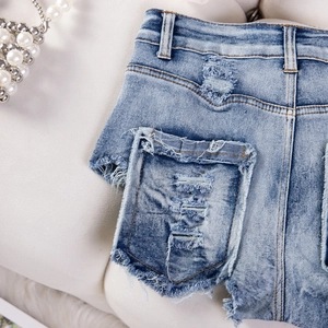 Dettaglio di pantaloncini in denim azzurro con bordi sfrangiati e strappi consumati