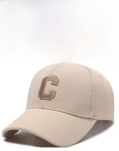 Detail of embroidered letter C on beige baseball cap with structured brim and fabric texture