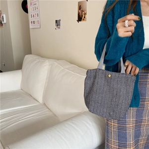 Close-up of herringbone woolen lunch bag with gold button detail held by a model