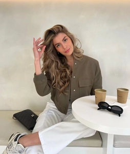 Army green cropped utility jacket and white straight trousers in a cafe setting
