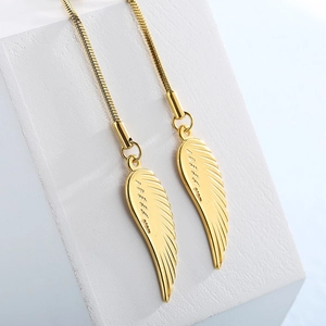 Elegant gold feather wing earrings with long snake chain pendants on a white display stand