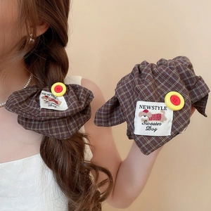 Close-up of brown plaid fabric scrunchie featuring a yellow button and embroidered dog label