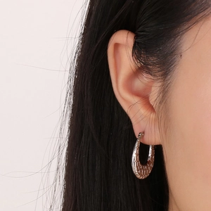 Close-up of silver-tone C-shaped earrings with textured hammered finish on a model