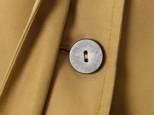 Detailed close-up of khaki twill fabric texture and matte black buttons on a short trench coat