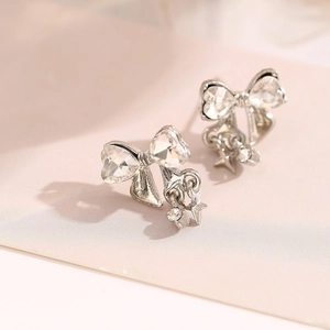 Close-up of silver bow earrings with heart-shaped crystals and hanging star pendants