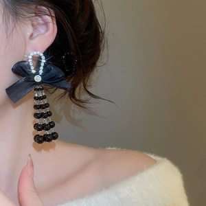 Detail of long drop earrings featuring a black bow, rhinestone horseshoe, and beaded tassels