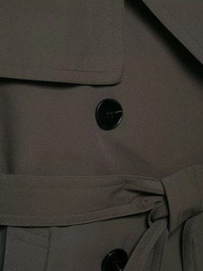 Detail of dark olive trench coat featuring a polished black button and matching belt strap
