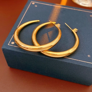 Close-up of golden C-shaped hoop earrings with zircon studs on blue jewelry box