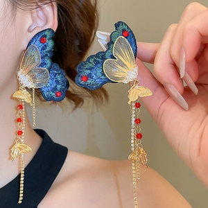 Détail des boucles d'oreilles papillon brodées avec ailes bleues et chaînes dorées