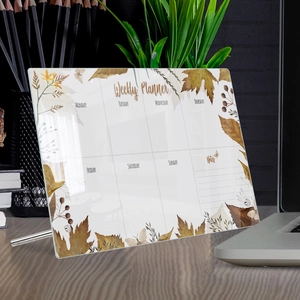 Close-up of acrylic weekly planner with autumn leaf design and metal stand on a desk