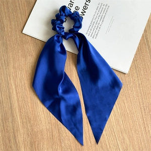 Detail of navy blue satin hair scrunchie with long ribbons on a minimalist desk