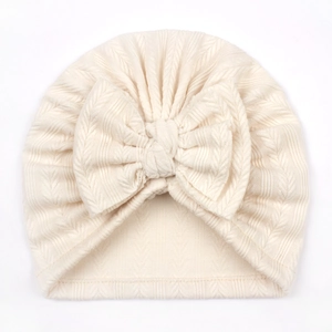 Detailed view of cream textured knit baby turban hat featuring a large soft front bow