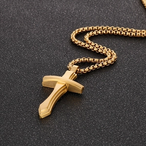 Détail d'un pendentif croix dorée 3D avec une chaîne box robuste sur surface noire