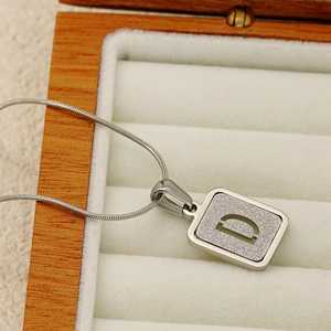Detail of silver stainless steel square pendant with letter D on a snake chain