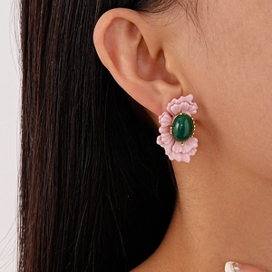 Detail of floral earring with pink petals and a green gemstone center on model