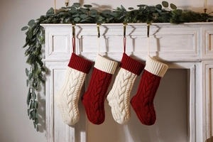 Detail of four knitted Christmas stockings in red and cream hanging on a decorated fireplace