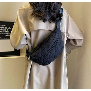 Quilted black crossbody chest bag with silver zipper shown on a beige trench coat