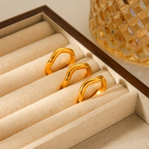 Detailed view of three gold-plated wavy geometric rings set in a linen jewelry tray