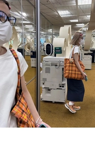 Detail view of large orange plaid tote bag with plush bear charm on a female shoulder