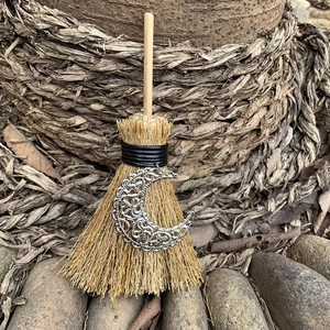 Detail of mini wicca broom with silver crescent moon charm and natural straw texture