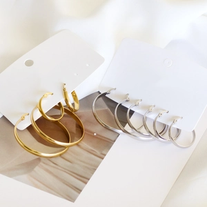 Various sizes of gold and silver stainless steel hoop earrings on white satin fabric