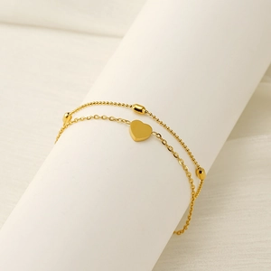 Detail of double-layer gold titanium steel anklet with heart charm and oval beads