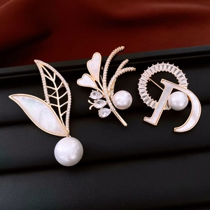 Detailed macro view of 14K gold-plated pearl brooches with zircon and shell inlay details