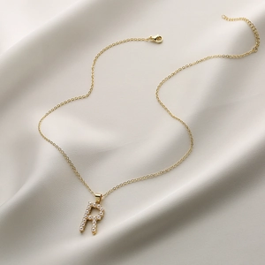 Dettaglio della collana dorata con ciondolo a lettera R e perle bianche incastonate