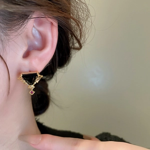 Détail macro d'une boucle d'oreille vintage avec gemme noire et goutte de zircon rouge