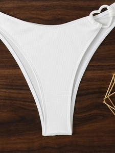 Dettaglio slip bikini bianco a costine con anello a cuore su sfondo in legno scuro