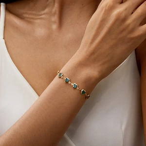 Detail of a gold chain bracelet with blue heart-shaped charms worn on a wrist