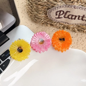 Three acetate daisy flower hair claws in yellow, pink, and orange on a white ceramic plate