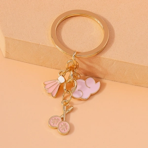 Close-up of golden keychain with pink badminton racket, shuttlecock, and cloud pendants
