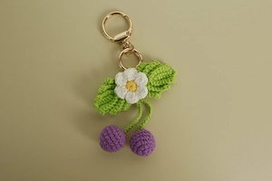 Dettaglio di portachiavi a ciliegia viola fatto a mano all'uncinetto con piccoli fiori