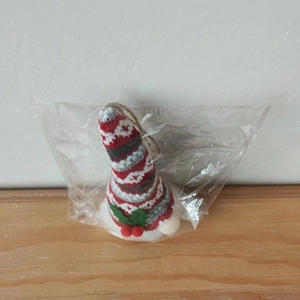 Detail of a knitted Christmas gnome ornament with red berries in transparent packaging