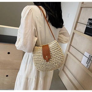 Detail of hand-woven beige paper straw saddle bag with brown leather strap and buckle