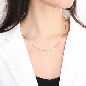 Detail showing a gold titanium necklace with white tube beads worn on a neck