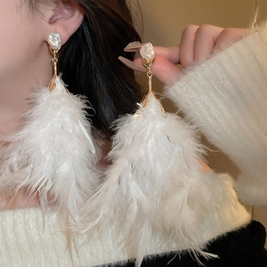 Close-up of elegant long white feather earrings with baroque pearl on a model