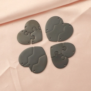 Vue détaillée de quatre pendentifs puzzle cœur gris foncé sur fond de tissu rose
